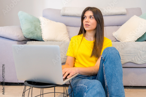 Woman with a computer sitting on a sofa, millennial looking at social networks, online blog or doing internet shopping at home