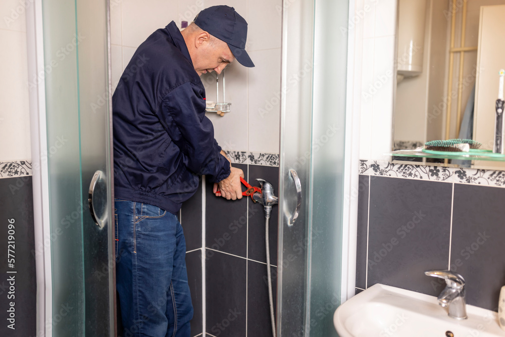 The mature plumber changing the shower faucet using work tool pliers, close-up photo. Plumbing, repairing, assemble concept. The mature plumber changing the shower faucet using work tool pliers, close-up photo. Plumbing, repairing, assemble concept.