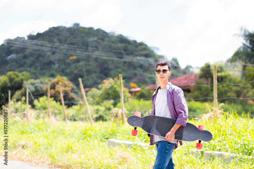 Man wearing plaid shirt and sunglasses holding a longboard and looking at camera. Man wearing plaid shirt and sunglasses holding a longboard and looking at camera.