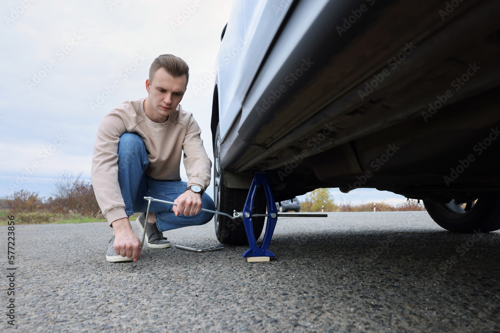 Young man changing tire of car on roadside