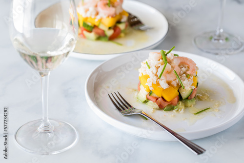 Crab and shrimp stack salads garnished with chives and served with white wine.