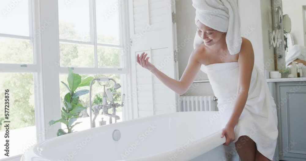 Happy asian woman running bath in bathroom, in slow motion