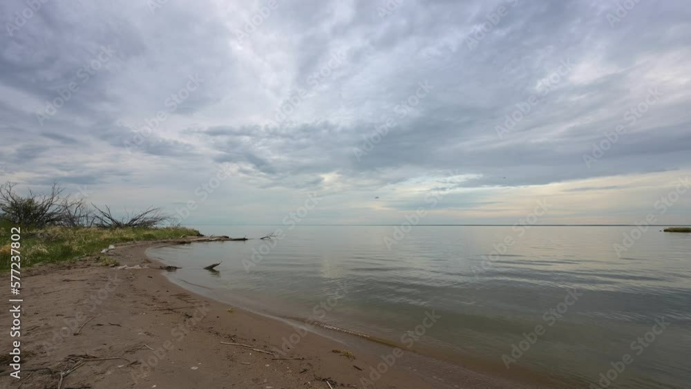Still setup on a small sandy beach next to a calm very large lake under a sky filled with bluish gray clouds.
Still setup on a small sandy beach next to a calm very large lake under a sky filled with bluish gray clouds.