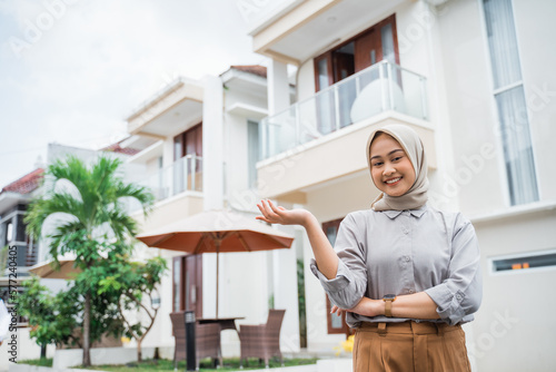 beautiful Asian woman in hijab with hand gesture presenting on residential background