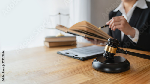 Asian female lawyer or legal advisor working on the scale of justice sitting at her desk and holding a pen to look at the information Detailed content about the scale of jurisprudence to study.