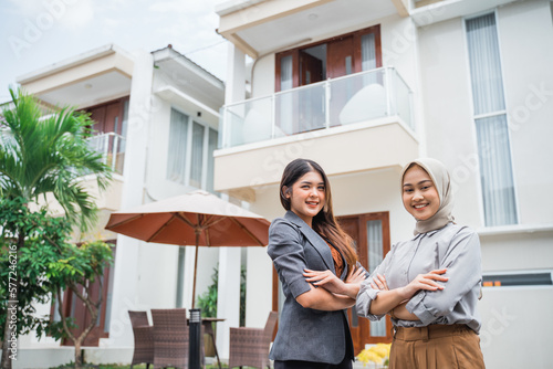 two female real estate agents smile with crossed arms in a residential background