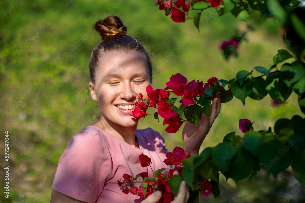 Portrait of happy beautiful girl, young positive woman is smelling beautiful yellow flowers in the garden, smiling, enjoying spring or summer day, breathing deep deeply fresh air Portrait of happy beautiful girl, young positive woman is smelling beautiful yellow flowers in the garden, smiling, enjoying spring or summer day, breathing deep deeply fresh air