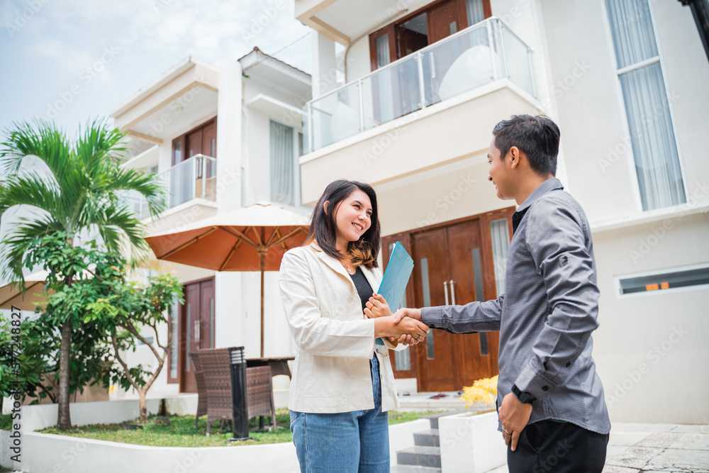 Asian female real estate agent shakes hands with prospective buyers in a residential background Asian female real estate agent shakes hands with prospective buyers in a residential background