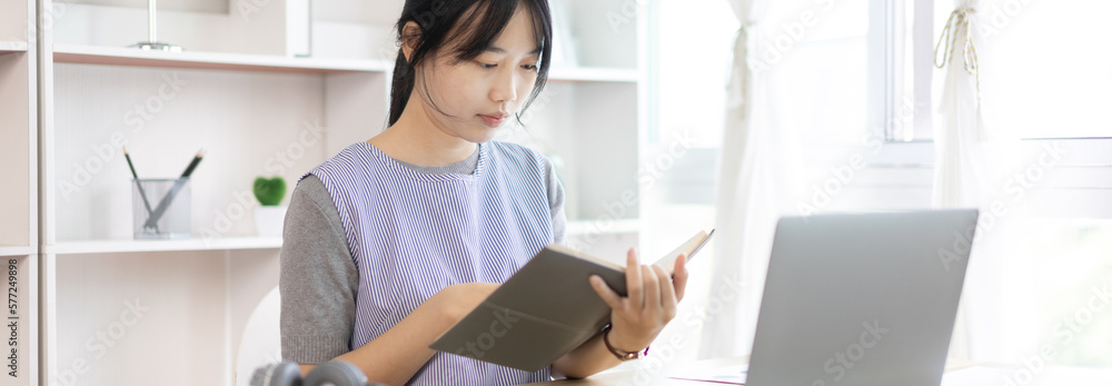 Asian woman taking notes in notebook while studying online in laptop at home, Video chat, Online communication , Stay home, New normal, Distance learning., Social distancing, Learn online.. Asian woman taking notes in notebook while studying online in laptop at home, Video chat, Online communication , Stay home, New normal, Distance learning., Social distancing, Learn online..