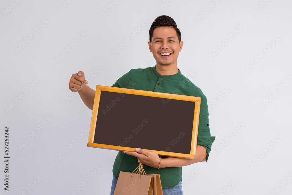 asian man pointing on the blackboard at his hand while bring the shopping bags on isolated background asian man pointing on the blackboard at his hand while bring the shopping bags on isolated background