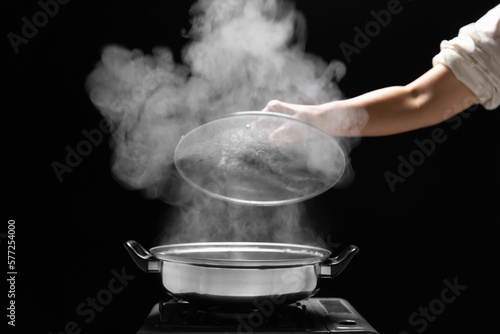 Steam over cooking pot in kitchen on dark background.