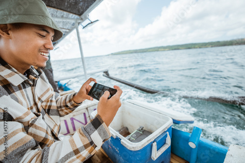 angler takes a photo of the box's fish storage contents with his cell phone while fishing at sea