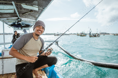 close up of smiling angler holding fishing rod while leaving for fishing with small fishing boat