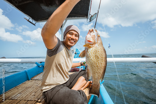 Foto Asian fisherman smiles as he catches a grouper while fishing on a small fishing