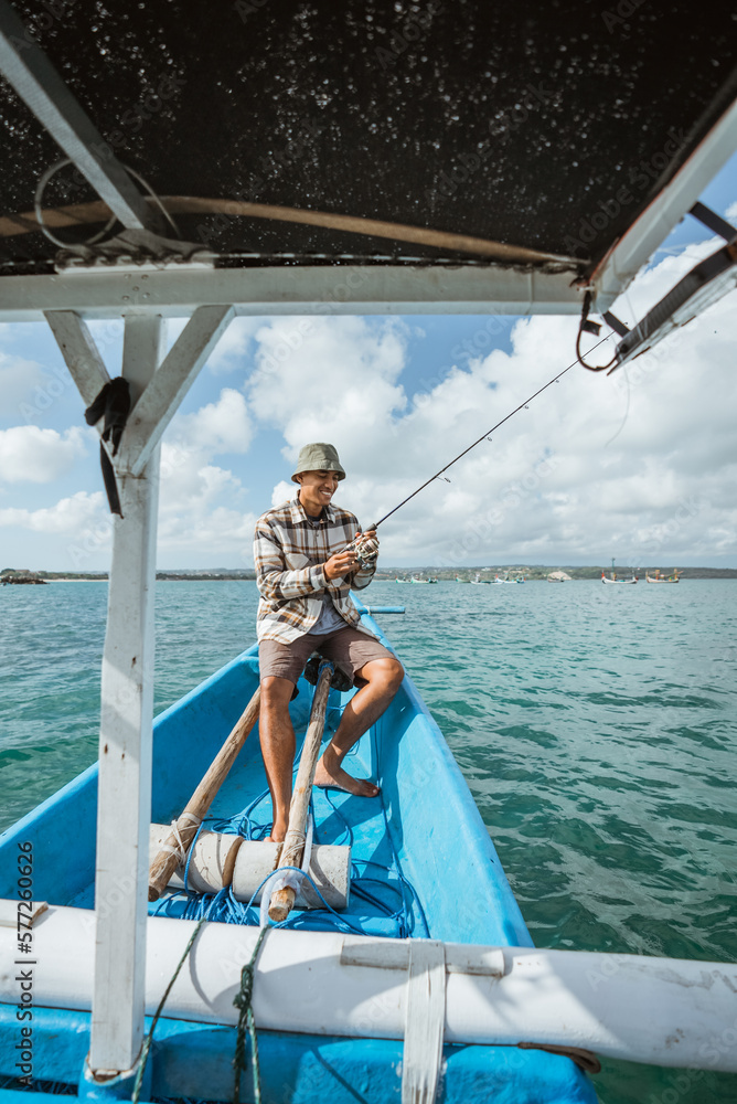 angler sitting at the front end of the boat while holding a fishing rod on a small fishing boat at sea