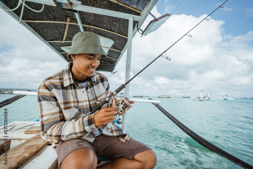 angler checking the reel before fishing with a fishing rod while on a small fishing boat angler checking the reel before fishing with a fishing rod while on a small fishing boat