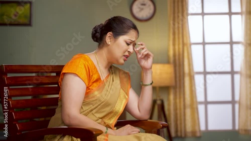 Deep thinking middle aged woman while sitting on chair at home - concept of unhappy, loneliness and worried or lost