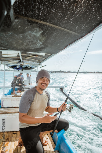 smiling fisherman holding a cell phone while fishing at sea with a small fishing boat