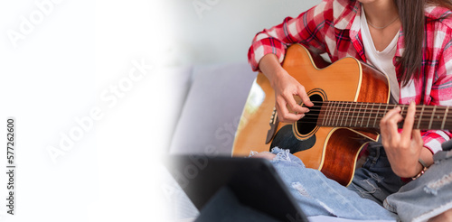Banner with blank copyspace, Concept of relaxation with music, Young woman plays acoustic guitar while learning music on tablet