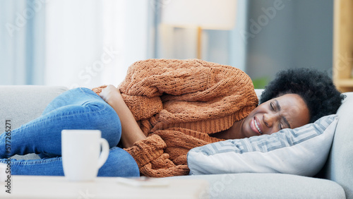 Fotografiet Woman with menstruation stomach cramps and belly ache holding her sore tummy while feeling ill on a sofa at home