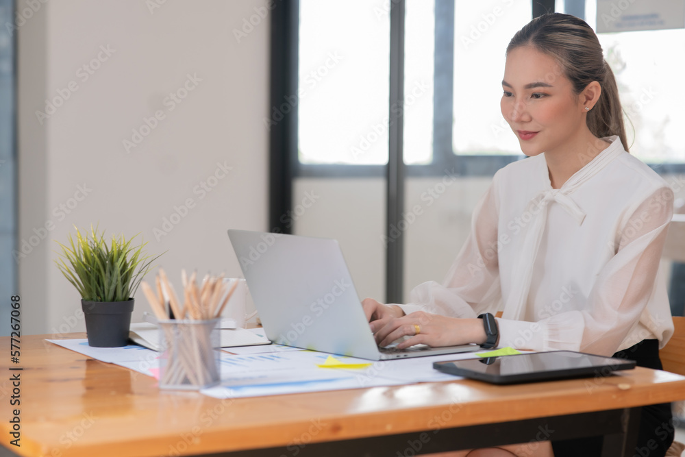 ฺAsia Businesswoman sitting and working using laptop to chat with customers online in office ฺAsia Businesswoman sitting and working using laptop to chat with customers online in office
