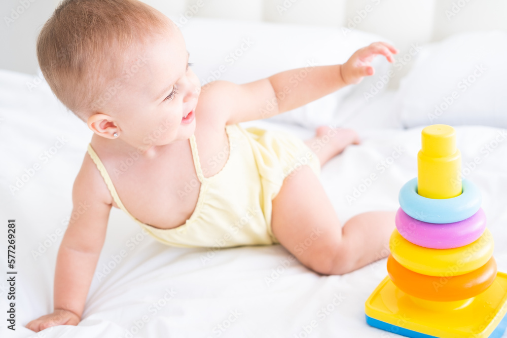 funny baby girl in yellow bodysuit playing with plastic toy children pyramid on bed funny baby girl in yellow bodysuit playing with plastic toy children pyramid on bed