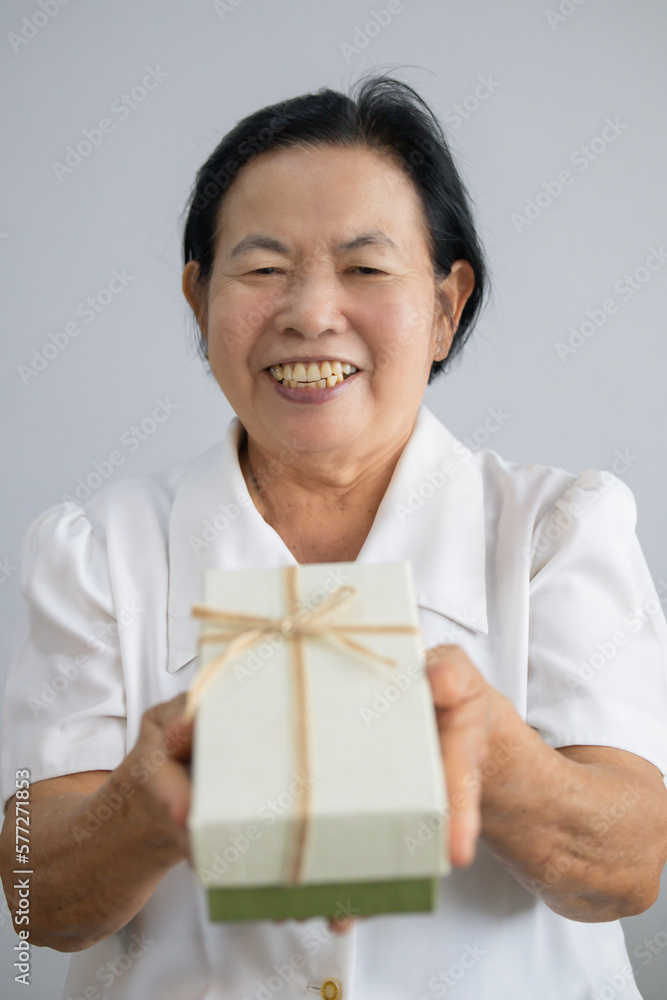 Asian elderly woman smiling and handing a gift box in front of her. Asian elderly woman smiling and handing a gift box in front of her.