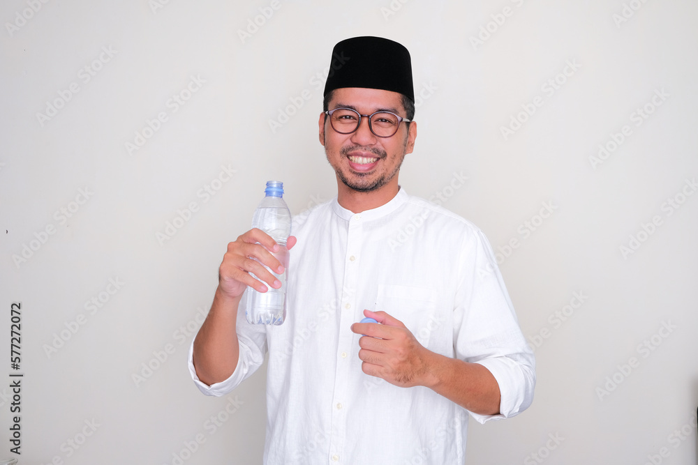 Moslem Asian man smiling at the camera while holding a bottle of drinking water Moslem Asian man smiling at the camera while holding a bottle of drinking water