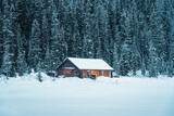 Snowy wooden cottage glowing in pine forest on Lake Louise in wintertime at Banff national park