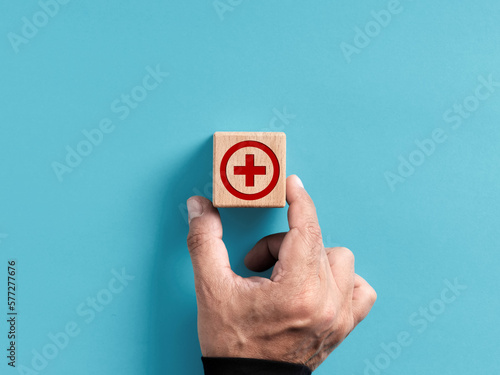 Health, healthcare and medical treatment concept. Hand places the wooden cube with medicine cross sign on blue background with copy space.