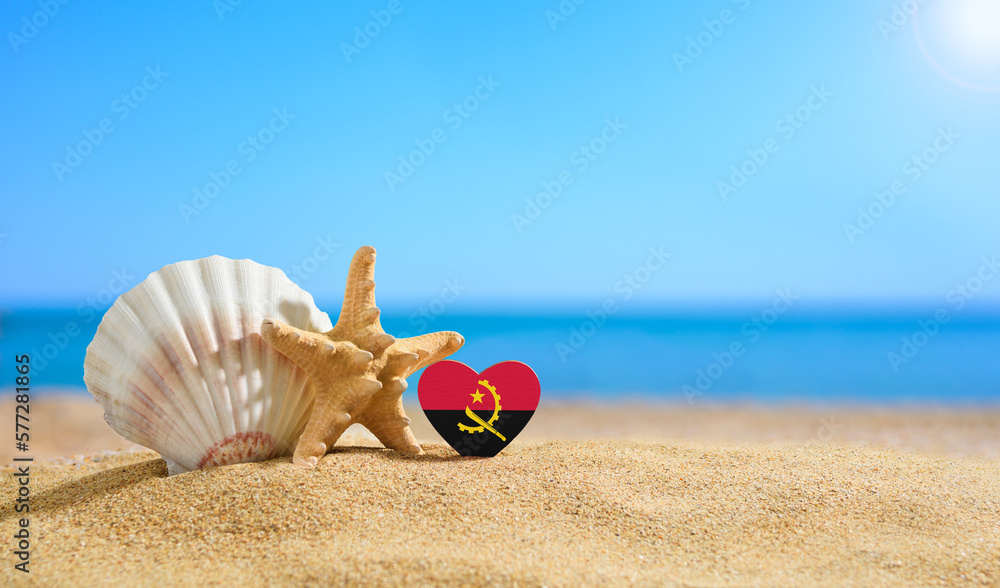 Obraz premium Beautiful beach in Angola. Flag of Angola in the shape of a heart and shells on a sandy beach.