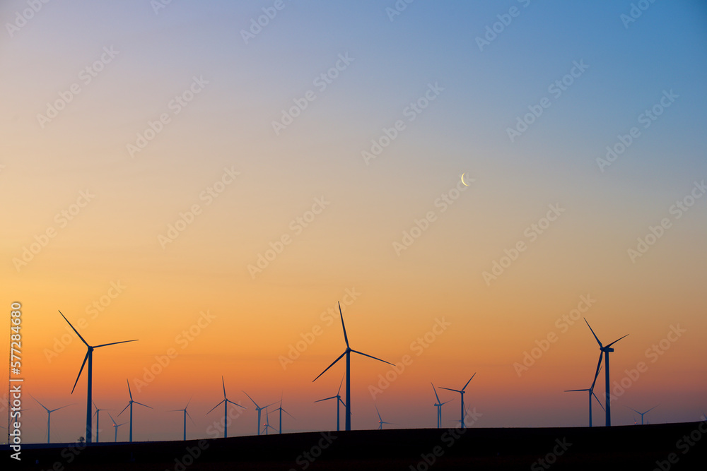 Silhouettes of a group of wind turbines at sunrise.