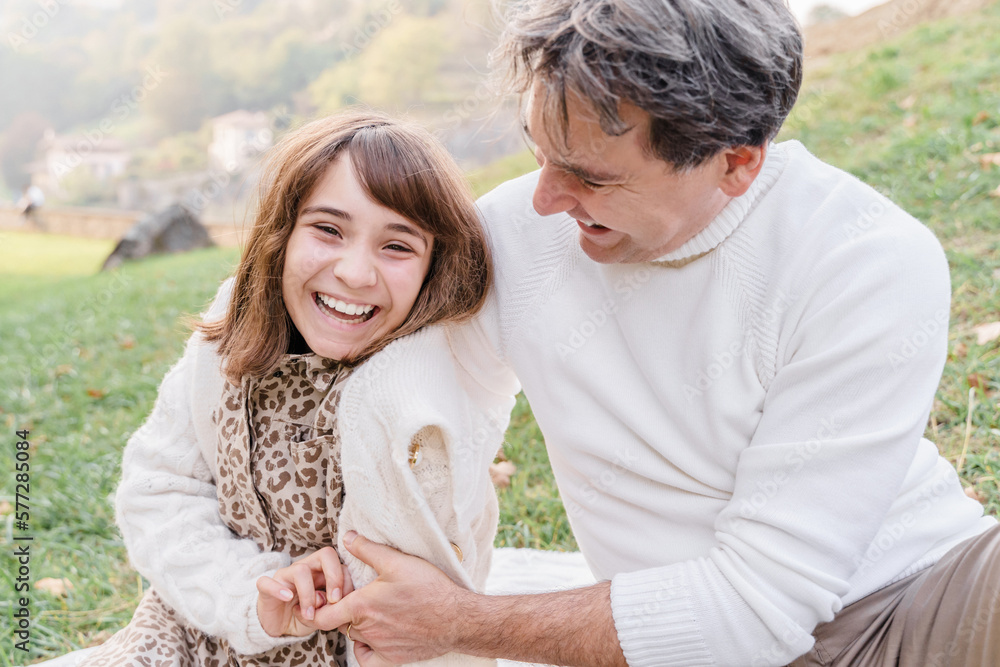 A man with and teenage daughter are sitting and hugging on the grass A man with and teenage daughter are sitting and hugging on the grass