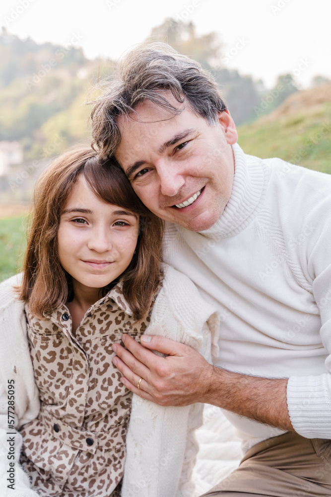 A man and teenage daughter are hugging and smiling outdoors