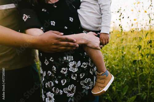 Pregnant mom holds toddler with dad in outdoor flower field