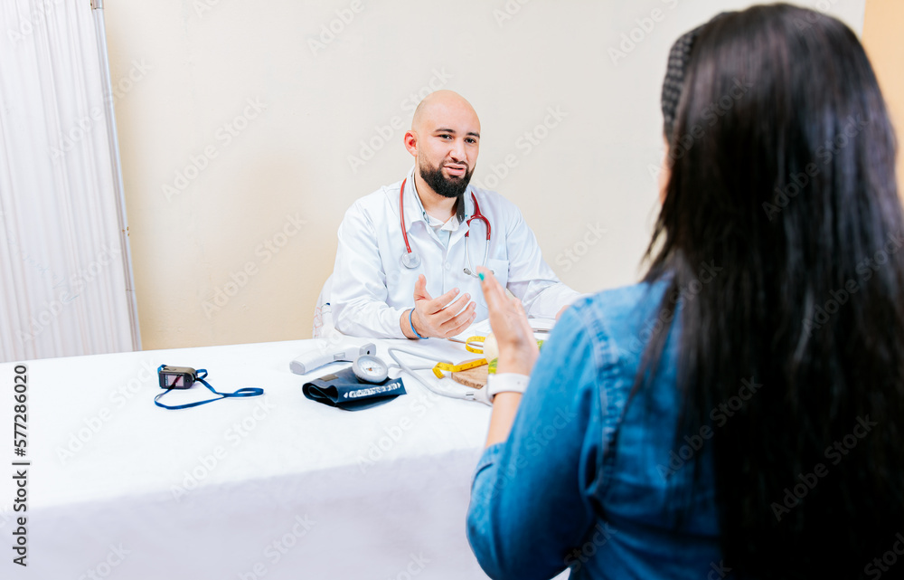 Back view of a female patient talking to the nutritionist. Smiling nutritionist explaining to a female patient, Nutritionist man talking to woman patient in office Back view of a female patient talking to the nutritionist. Smiling nutritionist explaining to a female patient, Nutritionist man talking to woman patient in office