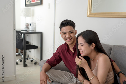 A cute asian couple spending time and sharing a laugh together while sitting in the sofa of their apartment.