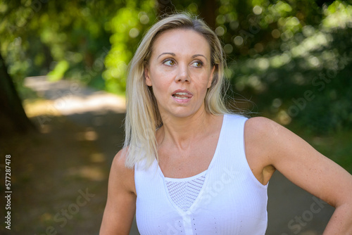 Blond woman standing biting her tongue deep in thought