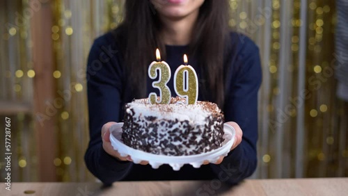 Birthday celebration concept. Happy woman holding birthday cake with burning candles number 39 and looking at the camera at home. Point of view or POV. Copy space photo