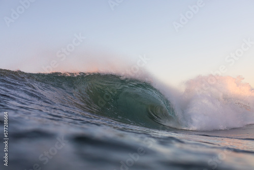 huge powerful wave crashing on a beach at sunrise