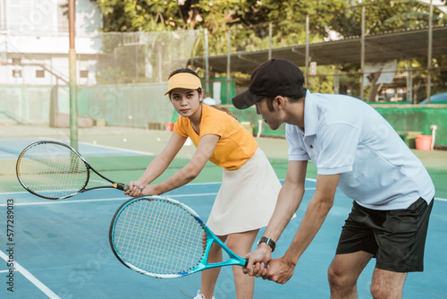 male trainer gives an example of a ready-to-receive ball position for a female player on the tennis court © Odua Images