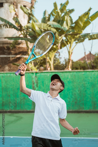 Excited men's singles athlete shouting and lifting racket on tennis court © Odua Images