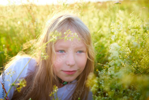 Portrait of pretty blonde girl having fun in a meadow on a natural landscape with grass and flowers on a sunny summer day. Portrait of a teenage child in summer or spring outdoors on field