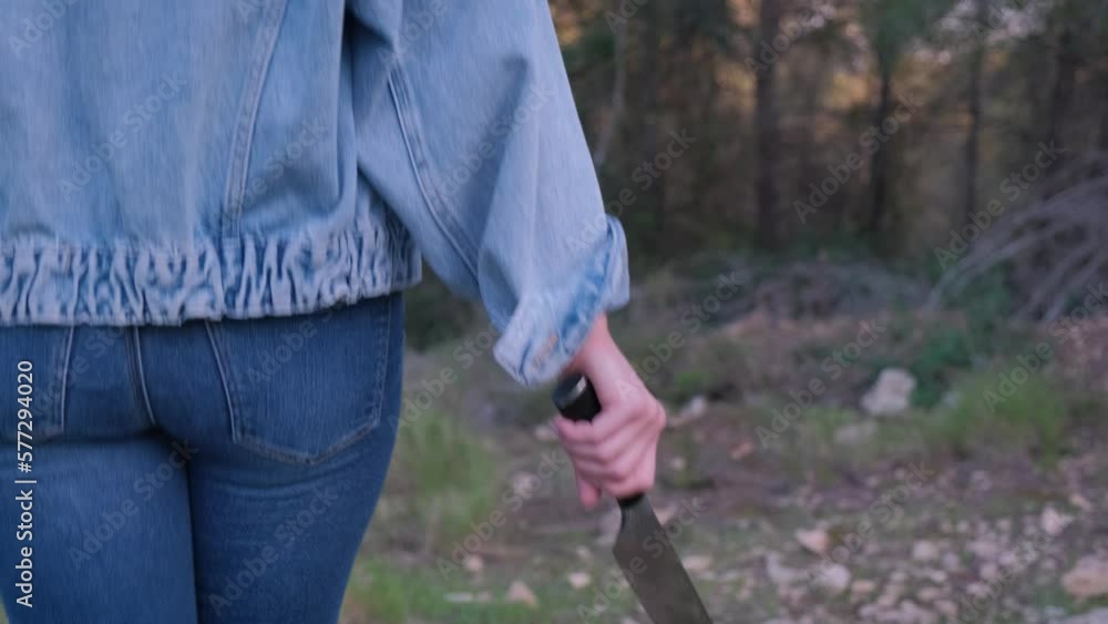 A girl in jeans with a knife in her hands walks through the forest.
