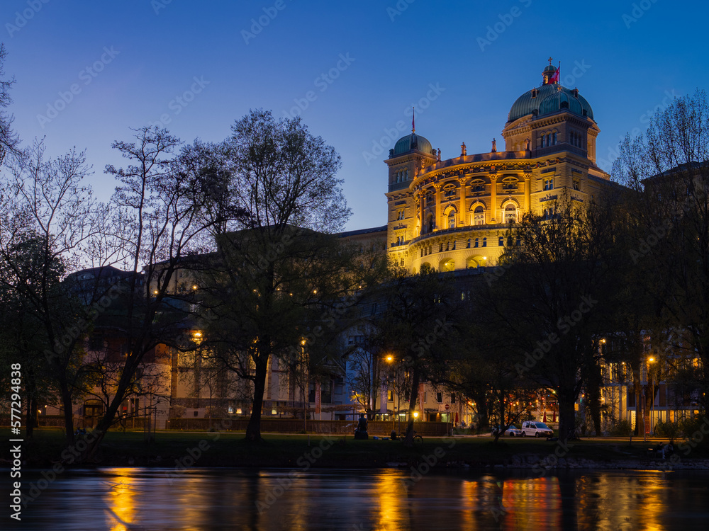 Berne, Switzerland - April 15th 2023: Evening view over the Aare river towards Bundeshaus, lighted during blue hour