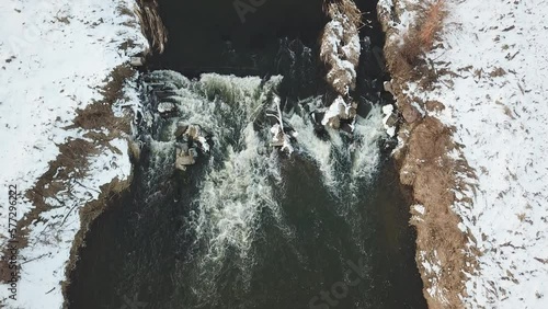 Waterfall on winter creek. Snow on frozen riverbanks. Top Aerial View Of River Cascade. Stream water flowing between rocks