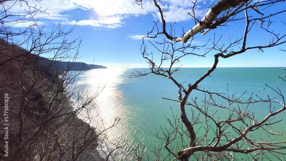 Panoramic view of the Black Sea coast from the mountain through the branches of trees. View of the blue water and the rocky seashore from the Kiselyov cliff. Sunset on the beach. 4K Panoramic view of the Black Sea coast from the mountain through the branches of trees. View of the blue water and the rocky seashore from the Kiselyov cliff. Sunset on the beach. 4K