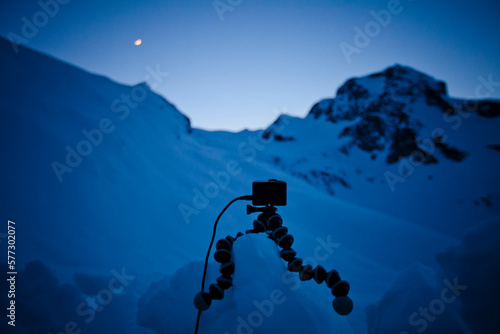 An HD camera sits on a tripod supportted by a block of snow, set up to capture a time-lapse of the night sky.