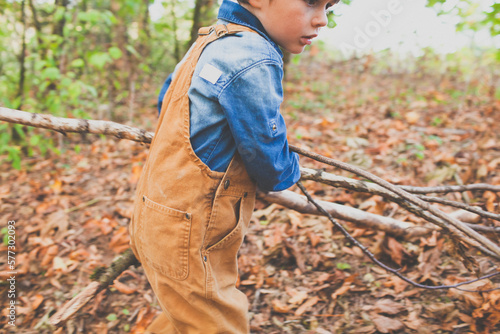 A young boy drags a tree branch out of the forest while playing in nature. photo