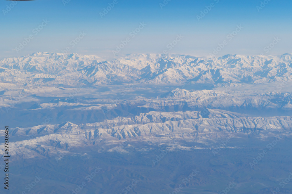 Fototapeta premium Wing of aerial view of an airplane jet flying above clouds from the window in traveling and transportation concept. White snow mountain in winter season. Nature landscape background.